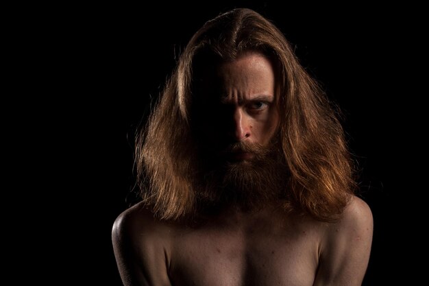 Hipster con pelo largo y barba sobre fondo negro en foto de estudio. expresión y moda