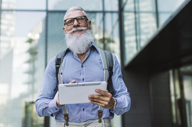 Hipster sênior segurando um tablet digital contra o edifício