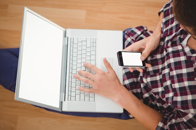 Hipster sentado com laptop usando smartphone