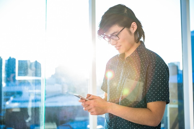 Hipster sonriente usando su teléfono en la oficina