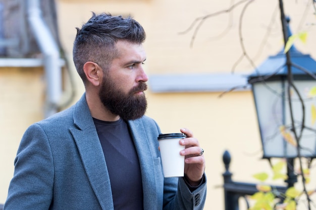 Hipster sostenga una taza de café de papel y disfrute del ambiente del parque Relajante descanso para tomar café Bébalo sobre la marcha Hombre barbudo hipster prefiere café para llevar Empresario barbudo bebe café al aire libre