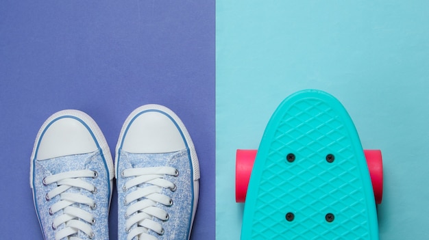 Hipster-Turnschuhe und Skateboard-Draufsicht auf lila blauem Hintergrund. Modekonzept des Minimalismus.