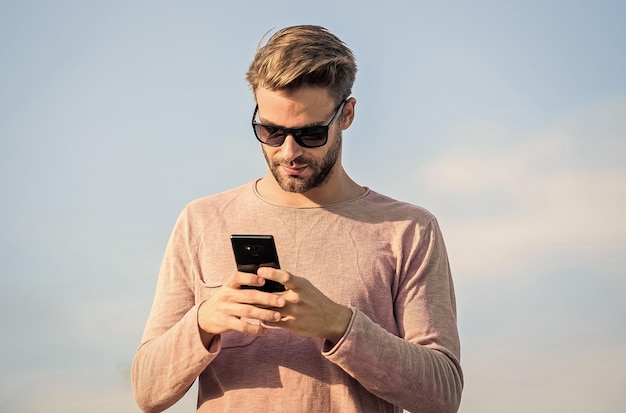 Hipster usa óculos de sol segurando o fundo do céu do telefone móvel Chamada de smartphone Hipster Chamada móvel do homem Fique em contato Conceito de chamada móvel Conversa móvel importante Aplicativo e internet