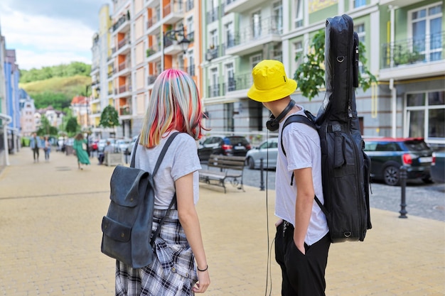 Hipsters adolescentes de moda chico y chica caminando hablando en la calle de la ciudad, chico con guitarra por si acaso. Juventud, estilo de vida, creatividad, comunicación, concepto de amistad.