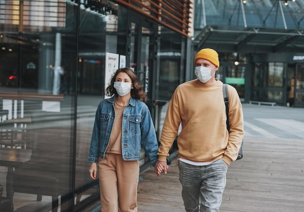 Foto hipsters de pareja de familia joven con estilo en máscara facial contra el edificio de vidrio nueva normalidad