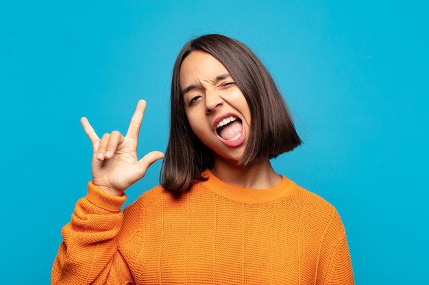 Hispanic Frau fühlt sich glücklich, lustig, selbstbewusst, positiv und rebellisch, macht Rock oder Heavy Metal Zeichen mit der Hand