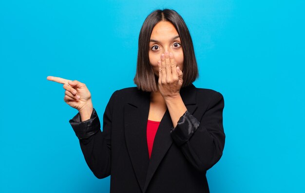 Hispanic Frau fühlt sich glücklich, schockiert und überrascht, bedeckt Mund mit der Hand und zeigt auf seitlichen Kopierraum