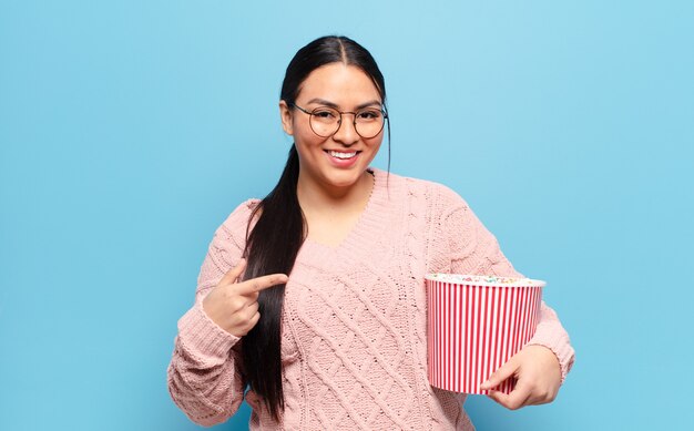 Hispanische Frau, die aufgeregt und überrascht aussieht und zur Seite und nach oben zeigt, um den Raum zu kopieren copy