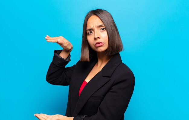 Hispanische Frau, die ein Objekt mit beiden Händen auf Seitenkopierraum hält, ein Objekt zeigt, anbietet oder bewirbt