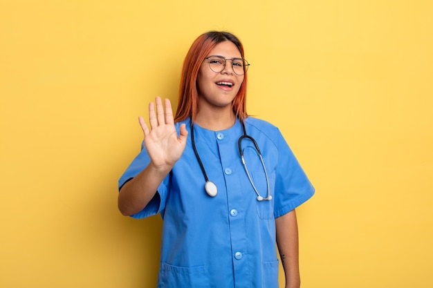 Hispanische Frau, die glücklich lächelt, mit der Hand winkt, Sie begrüßt und begrüßt. Krankenschwester-Konzept
