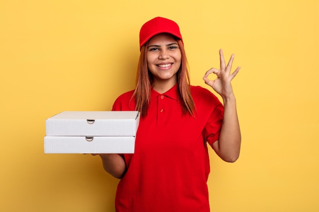 Hispanische Frau, die sich glücklich fühlt, wenn sie Zustimmung mit einer okay-Geste zum Mitnehmen zeigt, liefern Konzept