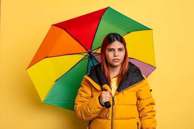 Hispanische Frau, die sich traurig, verärgert oder wütend fühlt und zur Seite schaut. Regen- und Regenschirmkonzept