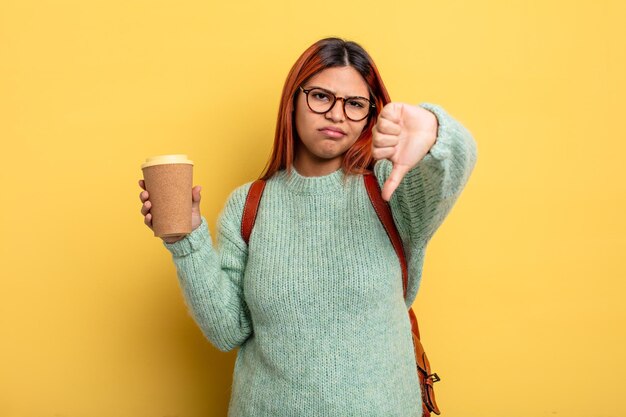 hispanische frau, die sich verärgert fühlt und den daumen nach unten zeigt. student mit einem kaffeekonzept