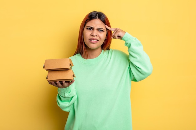 Hispanische Frau, die sich verwirrt und verwirrt fühlt und zeigt, dass Sie verrückt sind. Burger-Konzept zum Mitnehmen