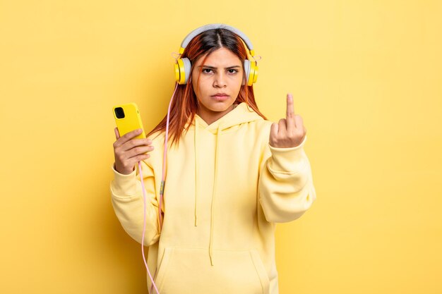 Hispanische Frau, die sich wütend, verärgert, rebellisch und aggressiv fühlt. Kopfhörer und Smartphone-Konzept