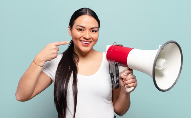 Hispanische Frau, die zuversichtlich lächelt, zeigt auf eigenes breites Lächeln, positive, entspannte, zufriedene Haltung