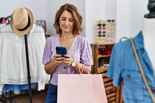 Hispanische Frau mittleren Alters mit Smartphone-Shopping im Bekleidungsgeschäft