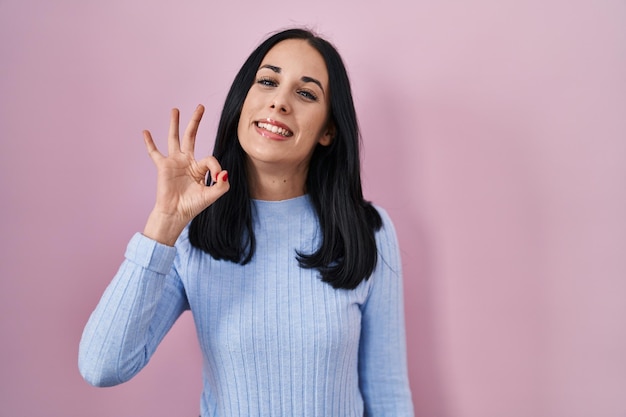 Hispanische Frau steht über rosa Hintergrund lächelnd positiv ok Zeichen mit Hand und Fingern erfolgreichen Ausdruck