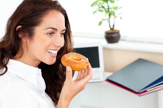 Hispanische Geschäftsfrau, die einen Donut in ihrem Büro isst