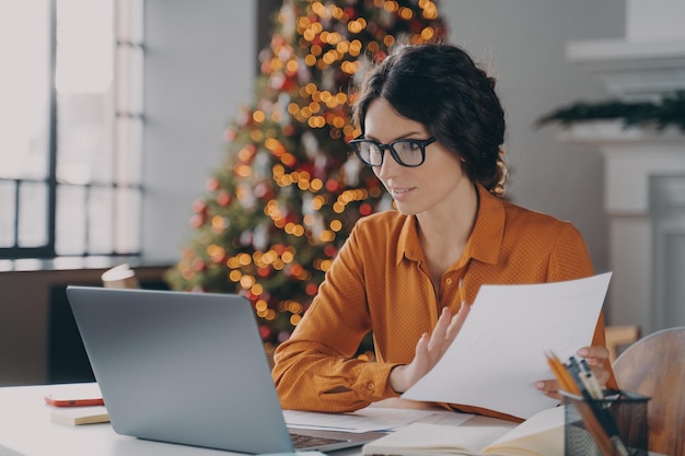 Hispanische Geschäftsfrau mit Brille, die an Weihnachten online im Büro arbeitet