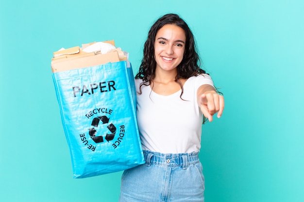 Hispanische hübsche Frau, die auf die Kamera zeigt, die Sie auswählt und eine Recyclingpapiertüte hält
