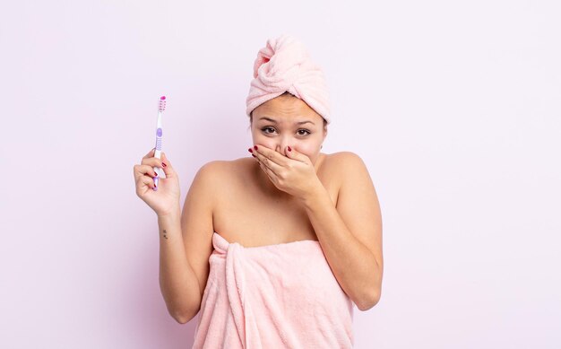 Hispanische hübsche Frau, die den Mund mit den Händen mit einem schockierten Zahnbürstenkonzept bedeckt