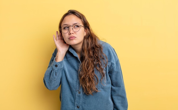 Hispanische hübsche Frau, die ernst und neugierig aussieht und zuhört, die versucht, ein geheimes Gespräch oder Klatsch zu hören