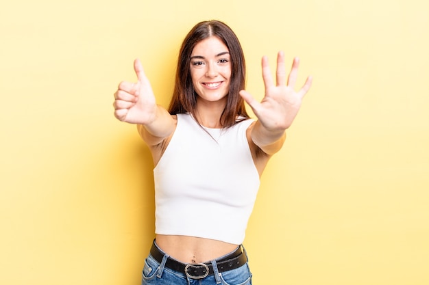 Hispanische hübsche frau, die lächelt und freundlich aussieht, die nummer sechs oder sechs mit der hand nach vorne zeigt und herunterzählt