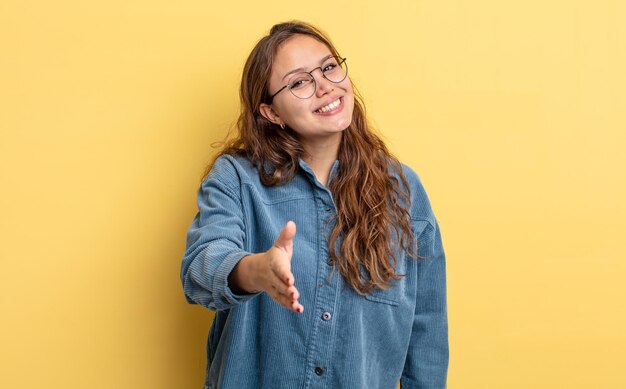 Hispanische hübsche Frau, die lächelt und glücklich, selbstbewusst und freundlich aussieht und einen Handschlag anbietet, um ein kooperierendes Geschäft abzuschließen