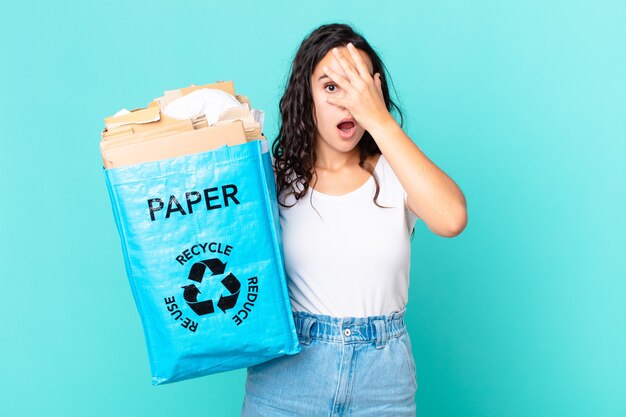 Hispanische hübsche Frau, die schockiert, verängstigt oder verängstigt aussieht, das Gesicht mit der Hand bedeckt und eine Recyclingpapiertüte hält