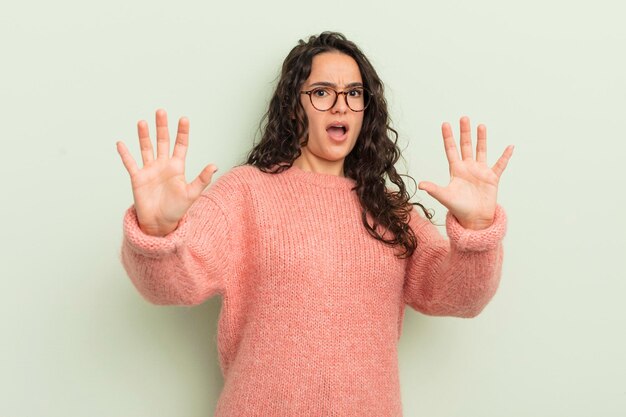 Hispanische hübsche Frau, die sich betäubt und verängstigt fühlt, weil sie etwas Beängstigendes mit offenen Händen fürchtet und sagt, bleib weg