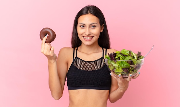 Hispanische hübsche Frau mit einem Donut und einem Salatdiätkonzept