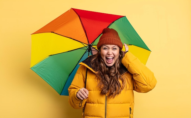 Hispanische hübsche Frau schreit mit den Händen in die Luft. Regenschirmkonzept