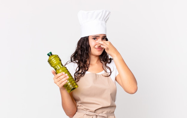 Hispanische hübsche Kochfrau, die eine Olivenölflasche hält