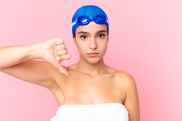 Hispanische hübsche Schwimmerin, die sich überquert und Daumen nach unten mit Schutzbrille zeigt