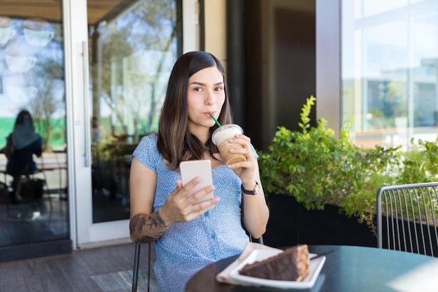 Hispanischer Food-Blogger trinkt Kaffee, während er Smartphone im Einkaufszentrum benutzt