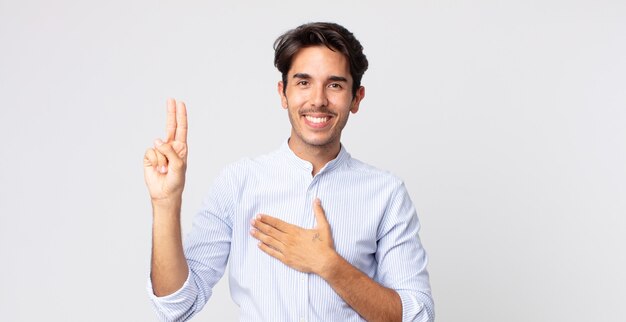 Hispanischer gutaussehender Mann, der glücklich, selbstbewusst und vertrauenswürdig aussieht, lächelt und ein Siegeszeichen zeigt, mit einer positiven Einstellung