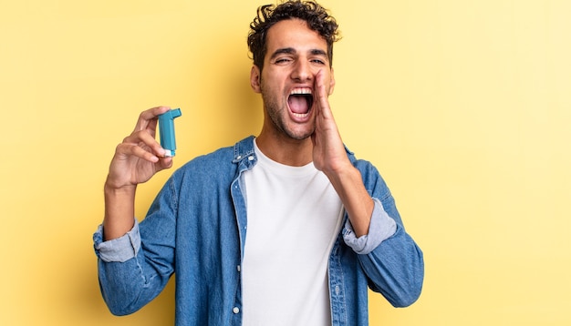 Hispanischer gutaussehender Mann, der sich glücklich fühlt und mit den Händen neben dem Mund einen großen Schrei ausstößt. Asthma-Konzept