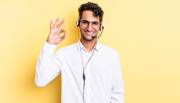 Hispanischer gutaussehender Mann, der sich glücklich fühlt und Zustimmung mit einer okayen Geste zeigt. Telemarketing-Konzept