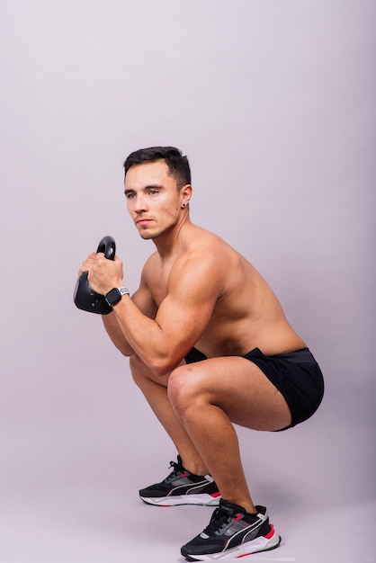 Hispanischer männlicher Athlet, der mit Kettlebell auf grauem Hintergrund Crossfit-Trainingsthema trainiert