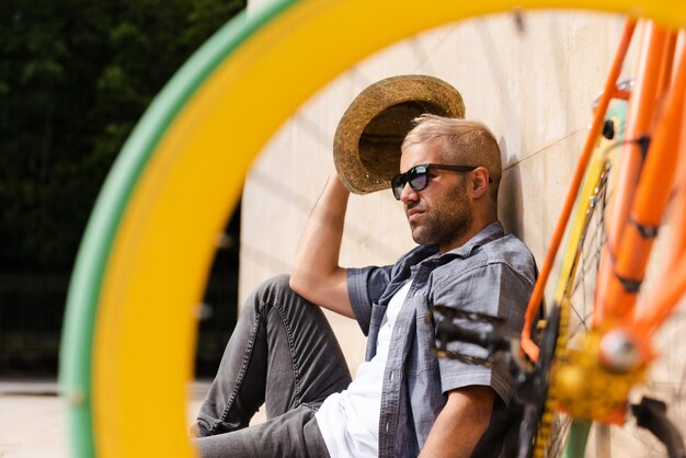 Hispanischer Mann, der sich hinter einem bunten Fahrrad an der Wand entspannt und sonnen kann.