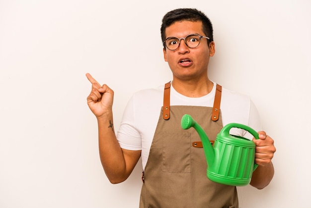 Hispanischer Mann des jungen Gärtners, der eine Gießkanne lokalisiert auf dem weißen Hintergrund hält, der zur Seite zeigt