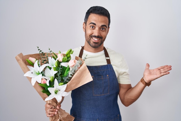 Hispanischer Mann mit Bart, der als Florist arbeitet und mit offenen Händen zur Seite zeigt, zeigt Kopierraum und präsentiert Werbung, die aufgeregt und glücklich lächelt