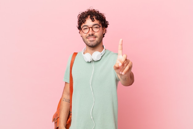 Hispanischer Student, der lächelt und freundlich aussieht, Nummer eins oder zuerst mit der Hand nach vorne zeigt, herunterzählt