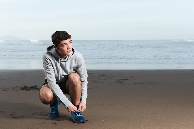 Hispanischer Teenager, der Laufschuhe am Strand bindet