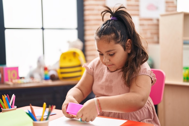 Hispanisches Mädchen in Übergröße, das mit Spielzeug spielt, das im Kindergarten auf dem Tisch sitzt