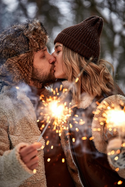 Historia de amor de pareja en el bosque nevado besándose y sosteniendo bengalas Pareja en la naturaleza invernal Pareja celebrando la fecha del día de San Valentín