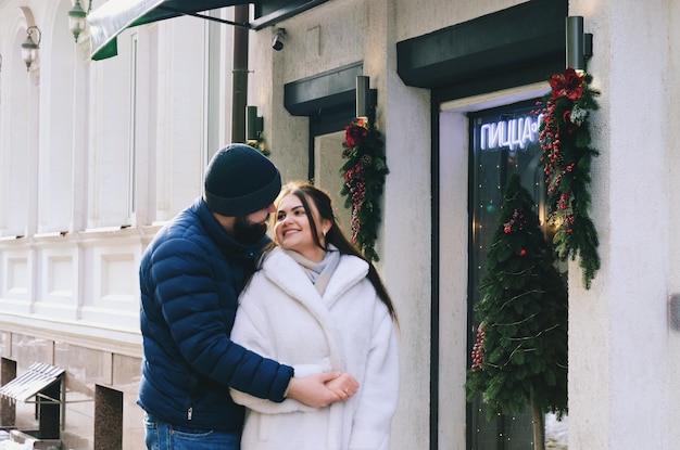 História de amor de casal andando na cidade de inverno nevado. Jovem de casaco azul com barba. mulher bonita