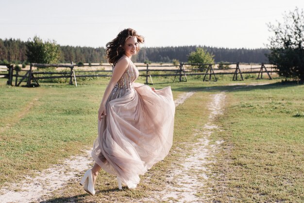 História de amor e casamento próximo ao pôr do sol. a noiva em um vestido claro e arejado é da cor de uma rosa empoeirada. vestido bege com brilhos. a noiva está correndo e sorrindo.