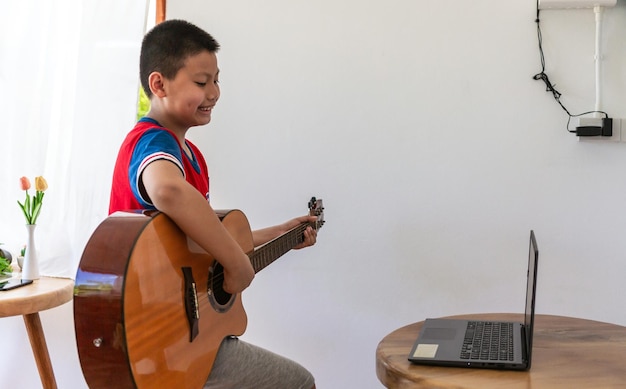 La historia de un niño mirando una computadora portátil mientras se prepara para practicar tocar la guitarra en casa